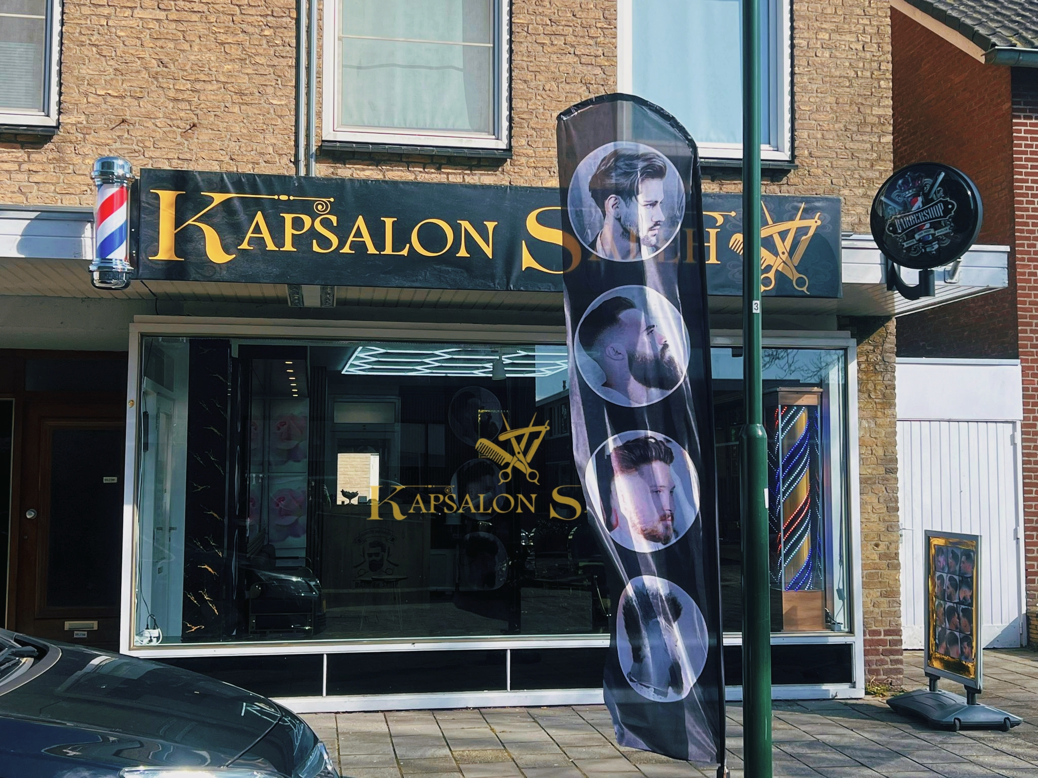 De gevel van Kapsalon Saleh aan de Burgemeester Remmenstraat: gouden letters, een kapperspaal en een vlag voor de deur