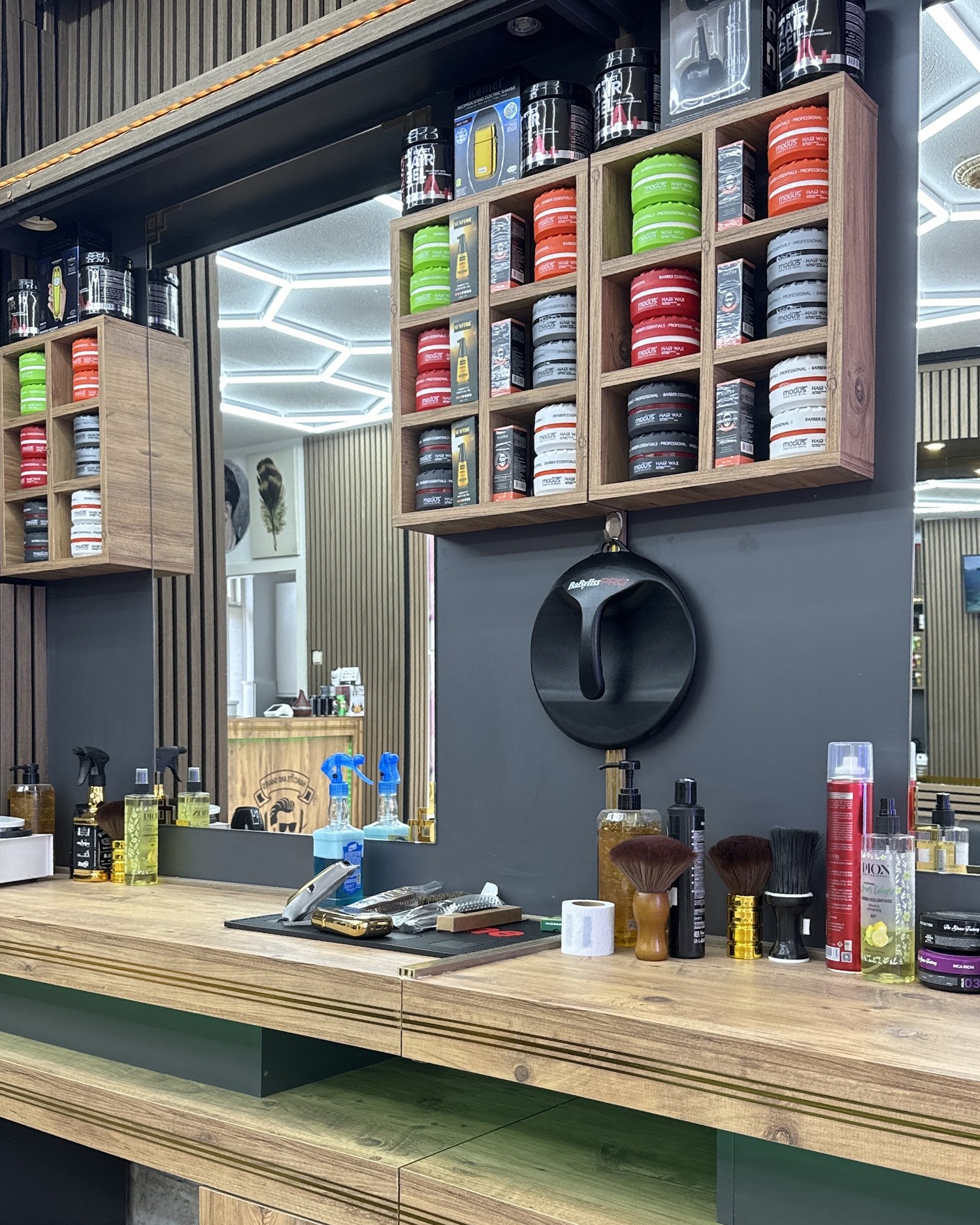 Een werkplek in de salon: houten schappen vol haarproducten, een ronde zwarte houder aan de wand en een houten werkblad met kwasten en tondeuses
